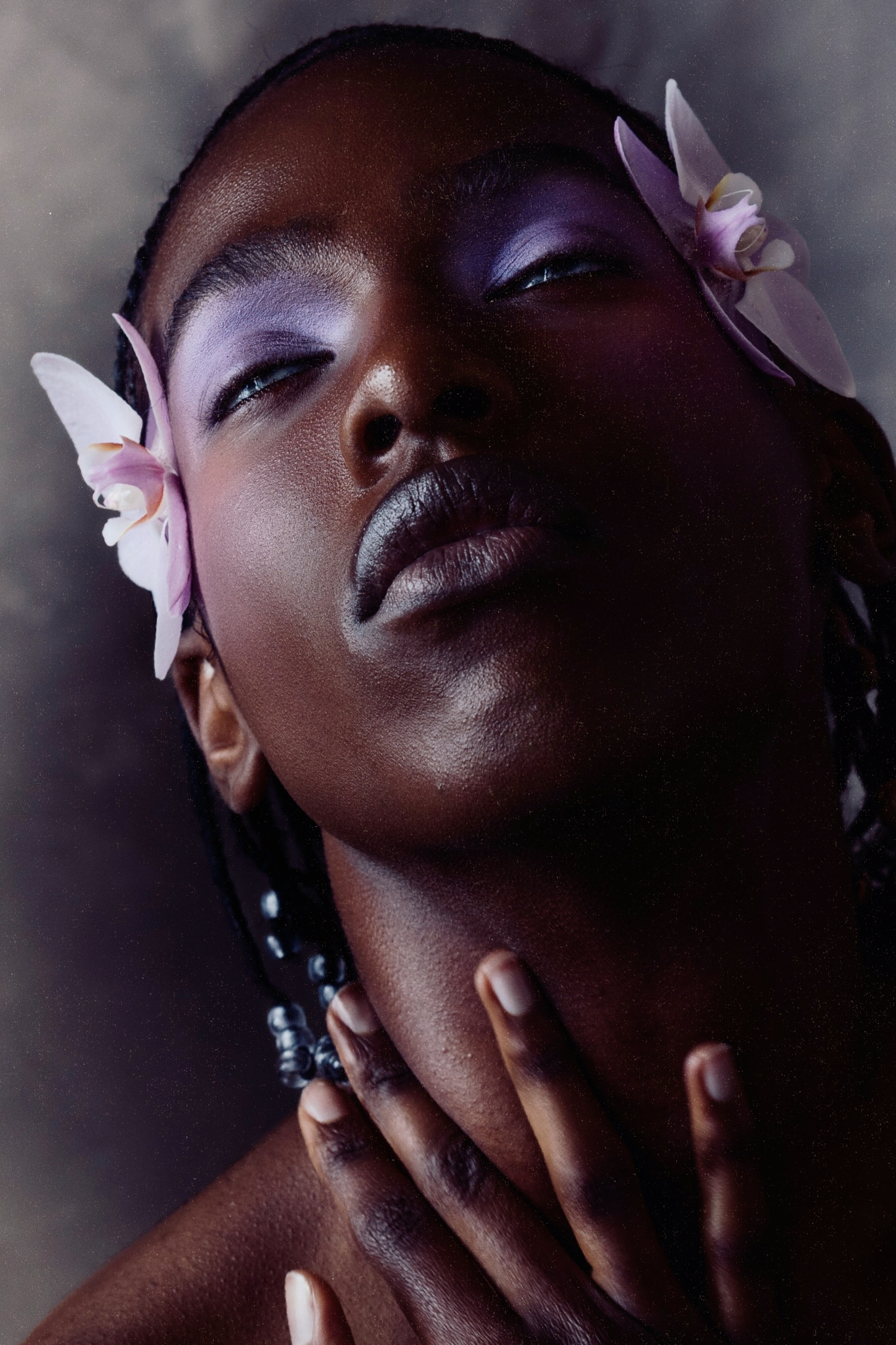 Close-up portrait of Black female model with purple eye makeup and pink orchid flowers in her hair.