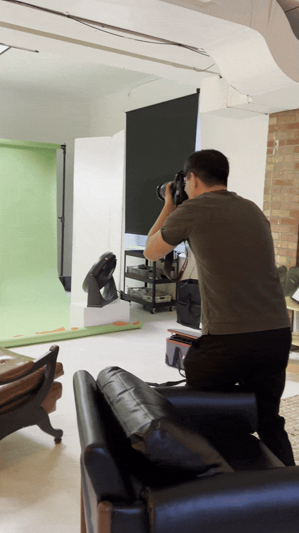 Photographer kneeling with camera in professional studio with green screen and black backdrop setup.