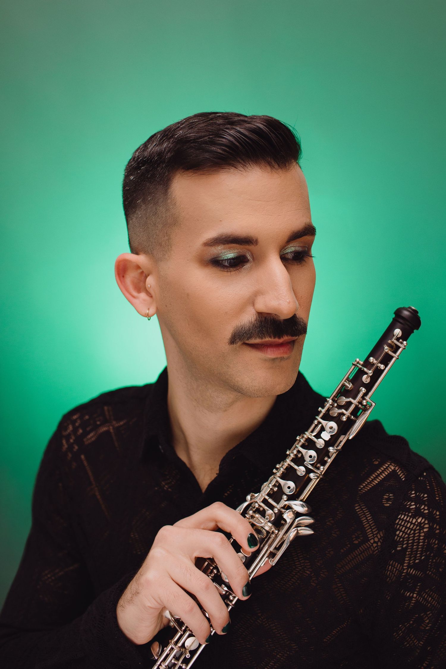 Musician with mustache holding an oboe instrument against a vibrant green background in a black shirt.