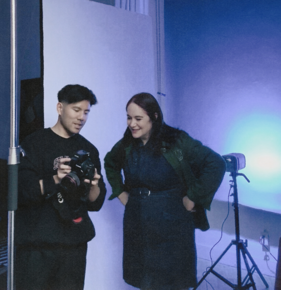 Photographer reviewing camera shots with female model in blue-lit photography studio.