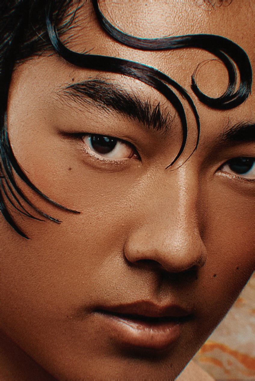 Close-up half-face portrait of an Asian man with artistic swirling black hair design framing his forehead.