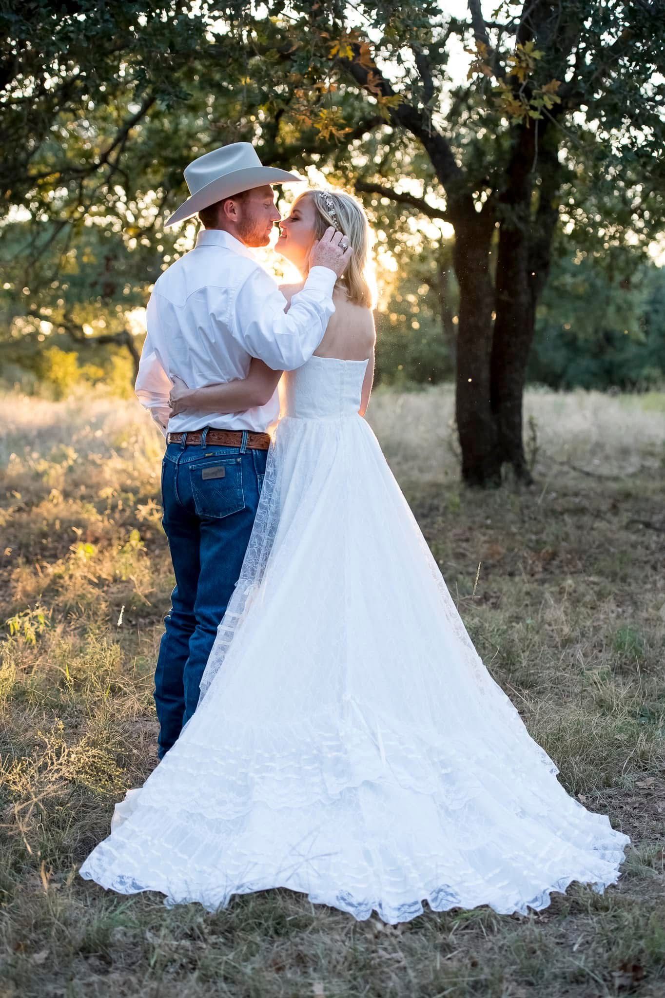 Bride and groom share a sunset kiss in a field, groom wearing cowboy hat and jeans.
