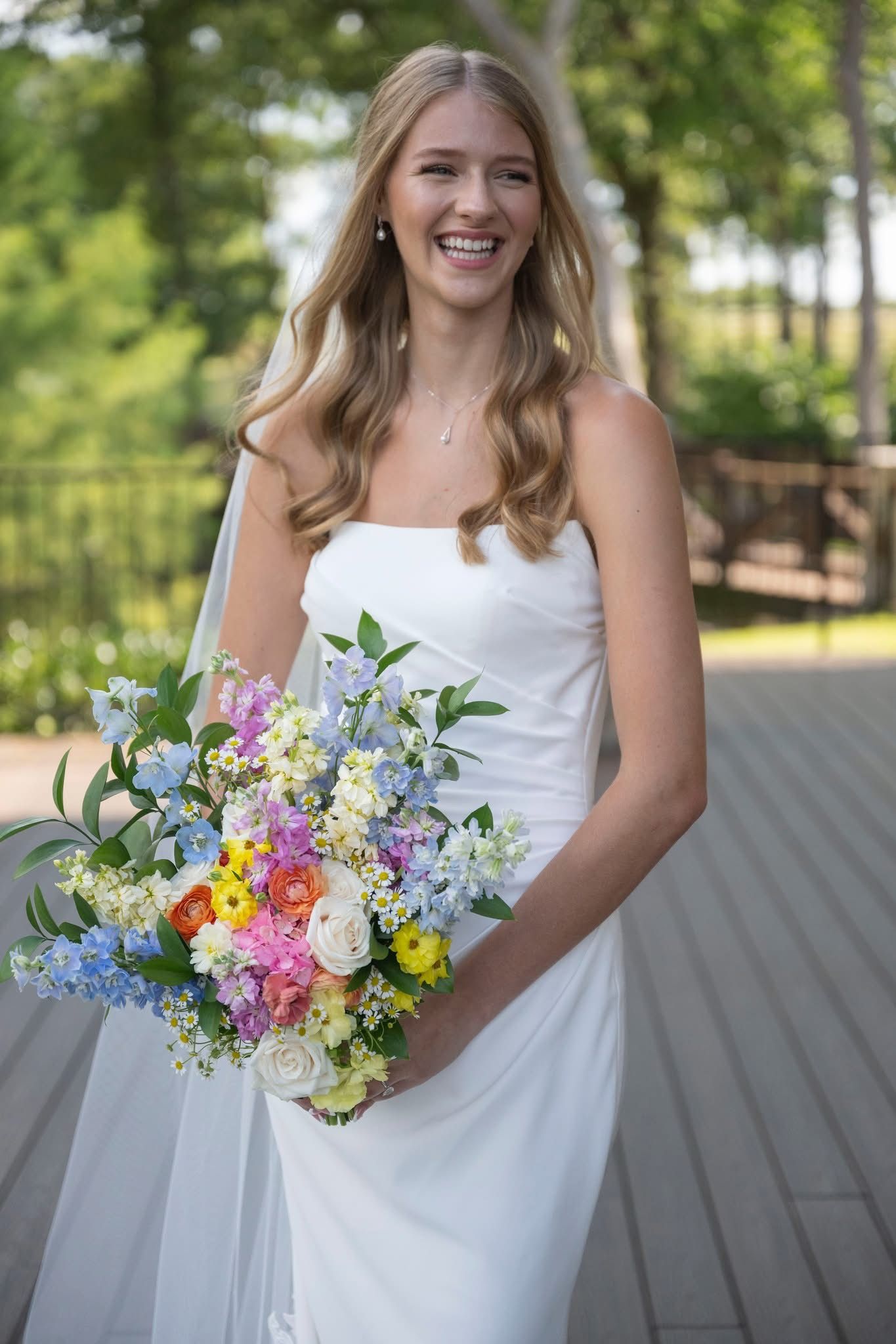 Joyful blonde bride in white strapless gown holding colorful spring bouquet smiling  at The Springs Alvarado Texas