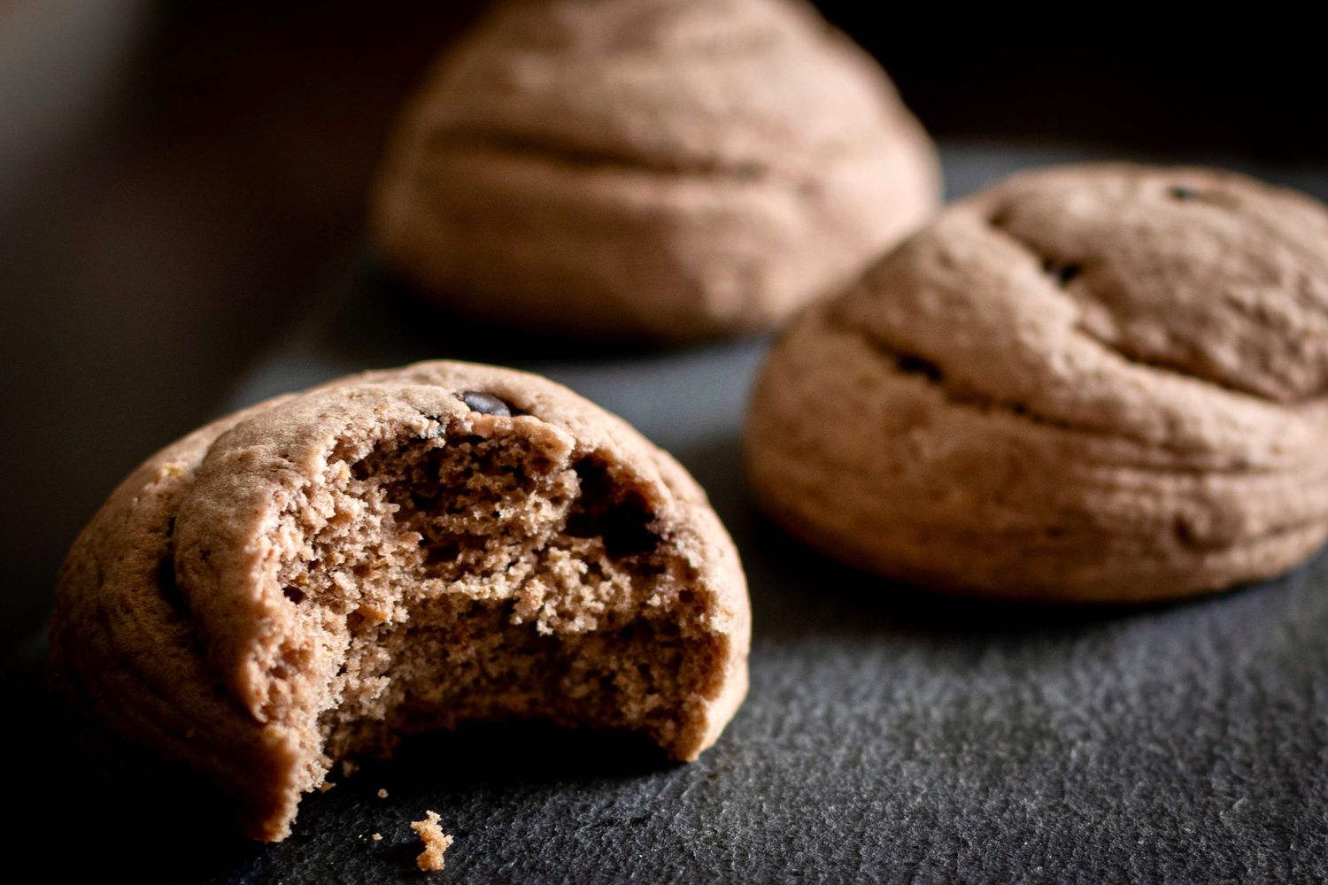 Chocolate cookies with one broken open showing soft interior on dark surface.