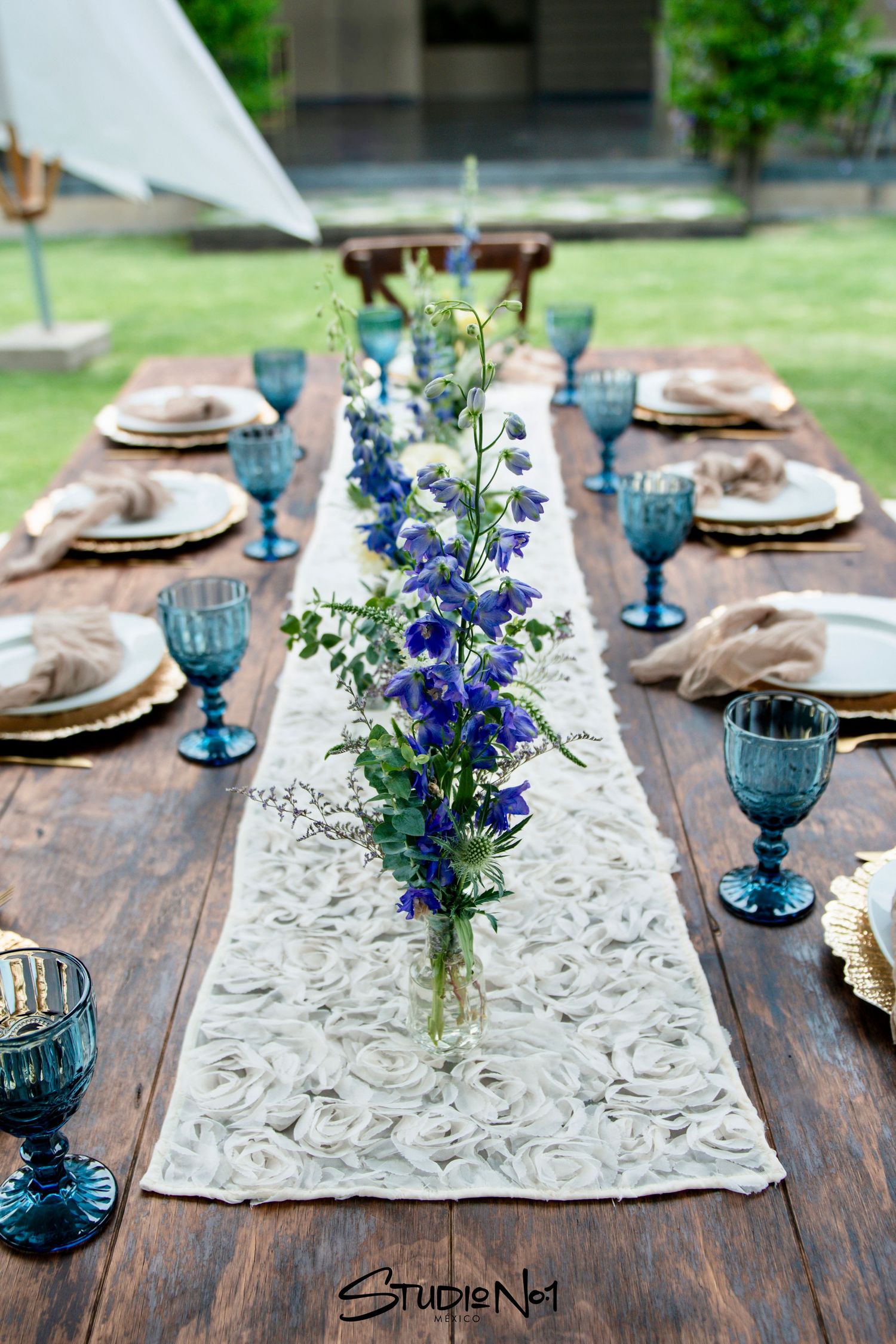 Rustic wooden wedding reception table with blue goblets, white runner, and blue delphinium centerpieces.