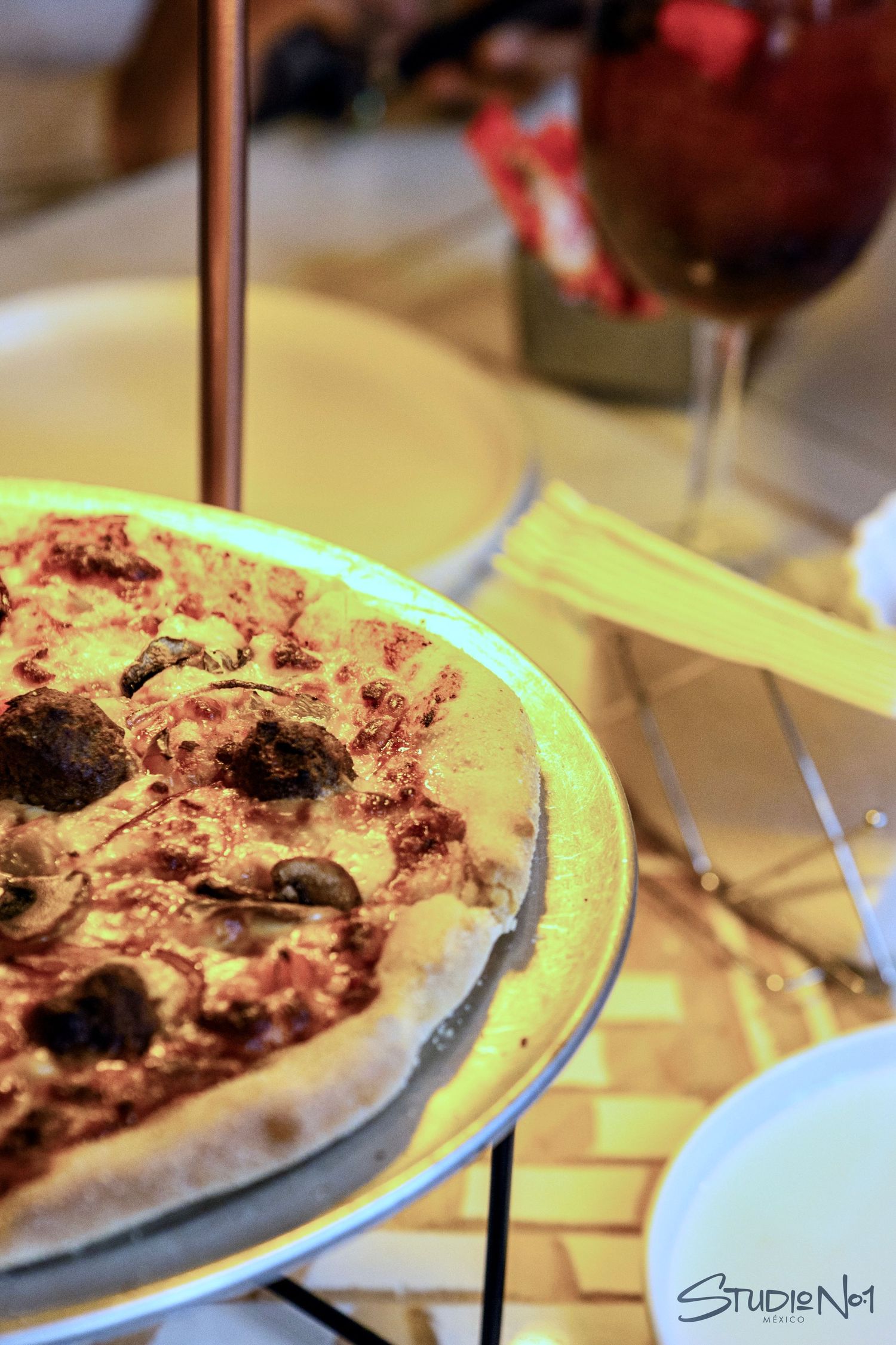 A freshly baked pizza topped with olives and tomato sauce served on a round pan at a restaurant table.