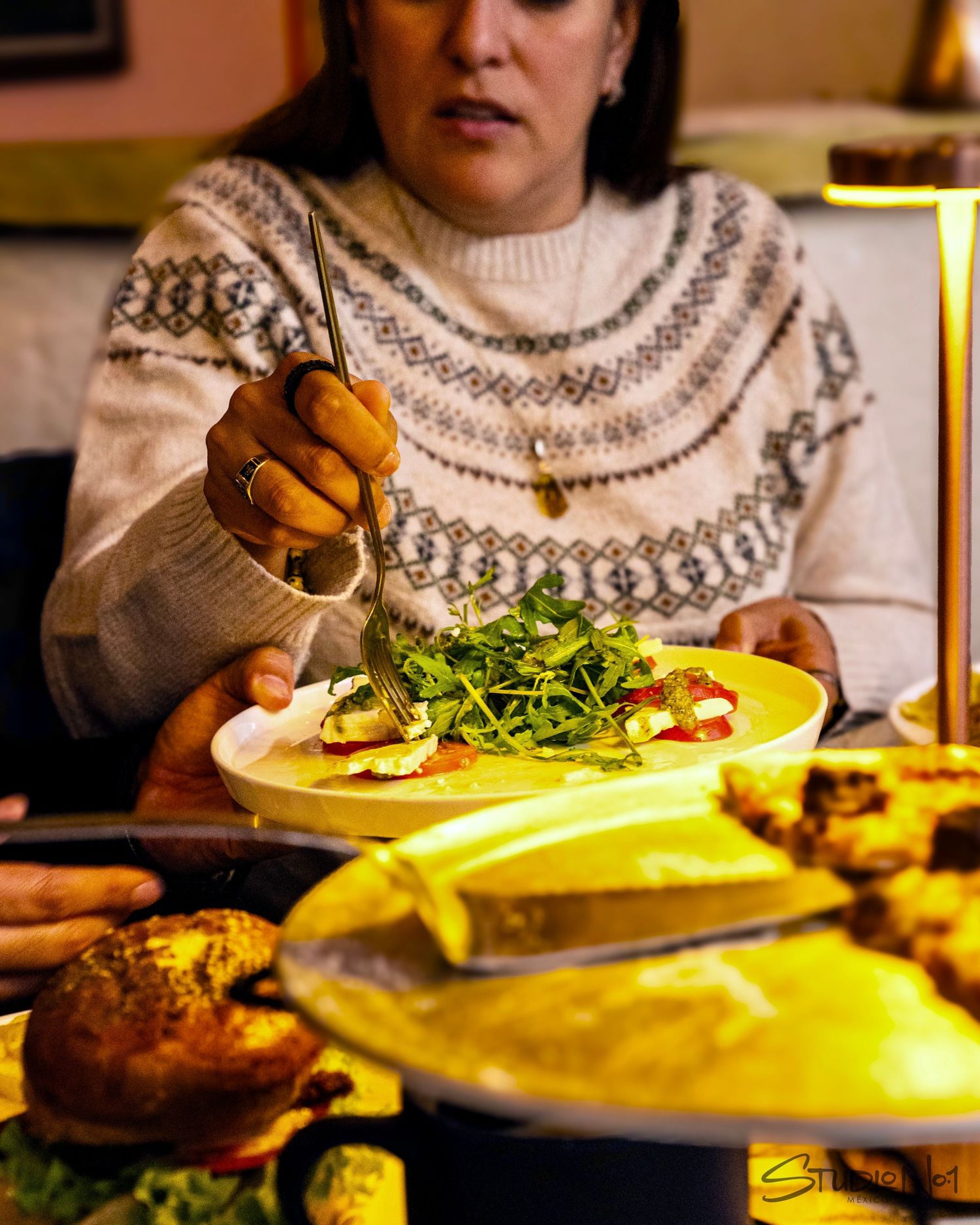 Woman in Nordic sweater eating fresh arugula salad at a warmly lit restaurant table.