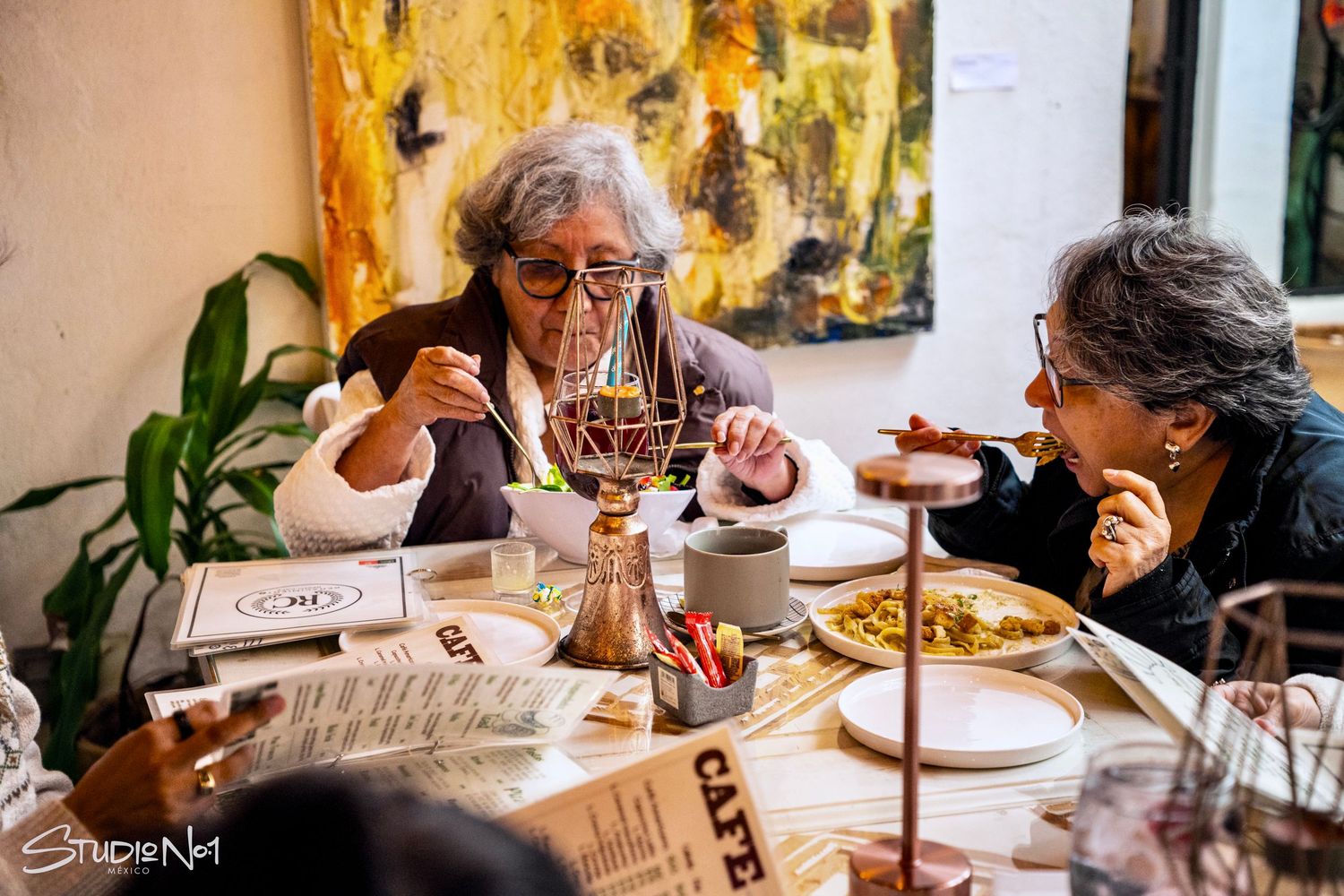 Two elderly women dining together at a restaurant, enjoying a meal surrounded by artwork and a warm ambiance.