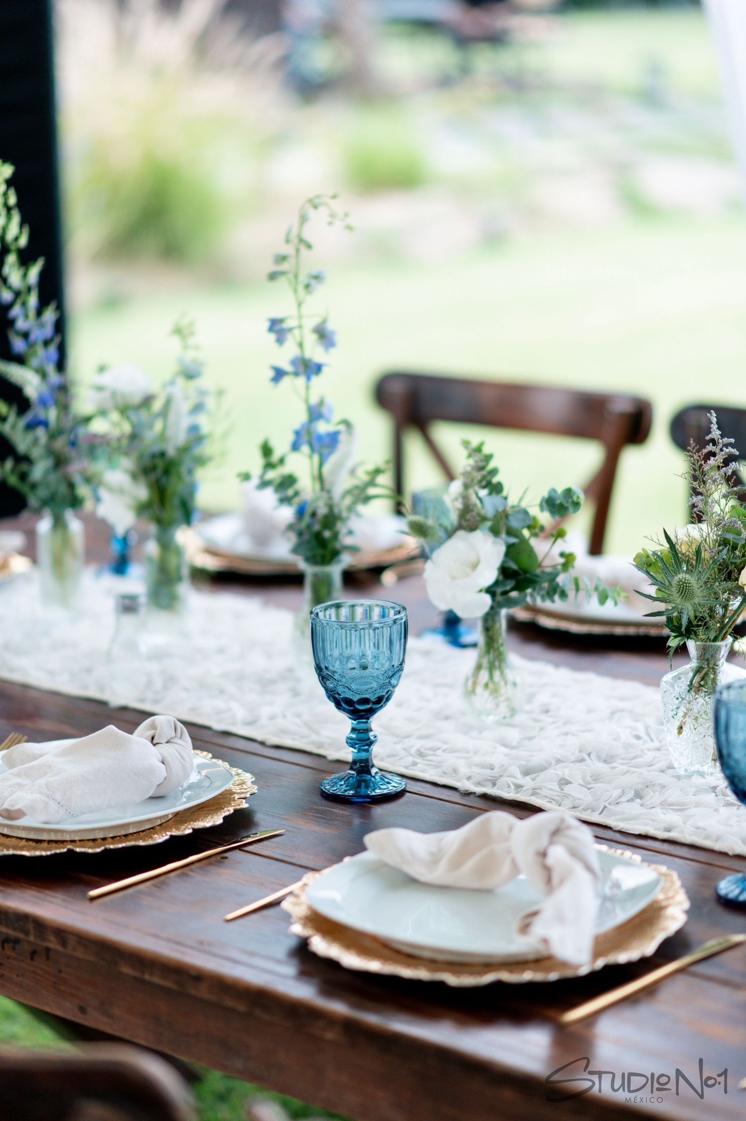 Elegant wedding table setting with blue goblets, white floral runner, and blue wildflower centerpieces.