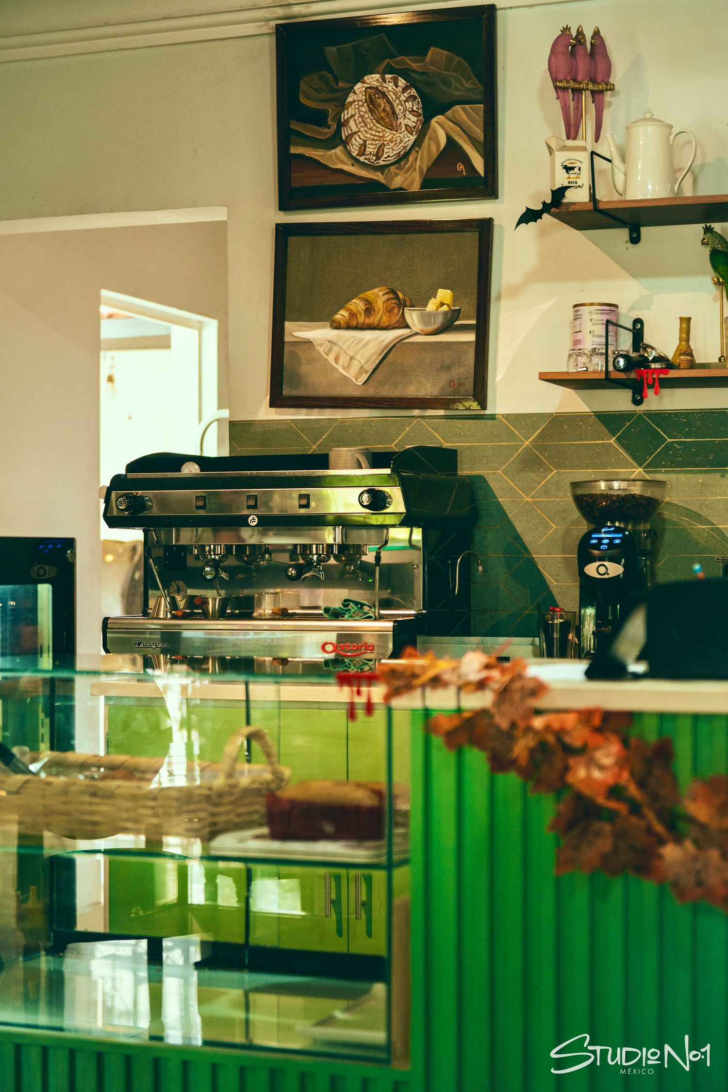 Cozy cafe interior with green counter, espresso machine, coffee grinder, and food paintings on the wall.