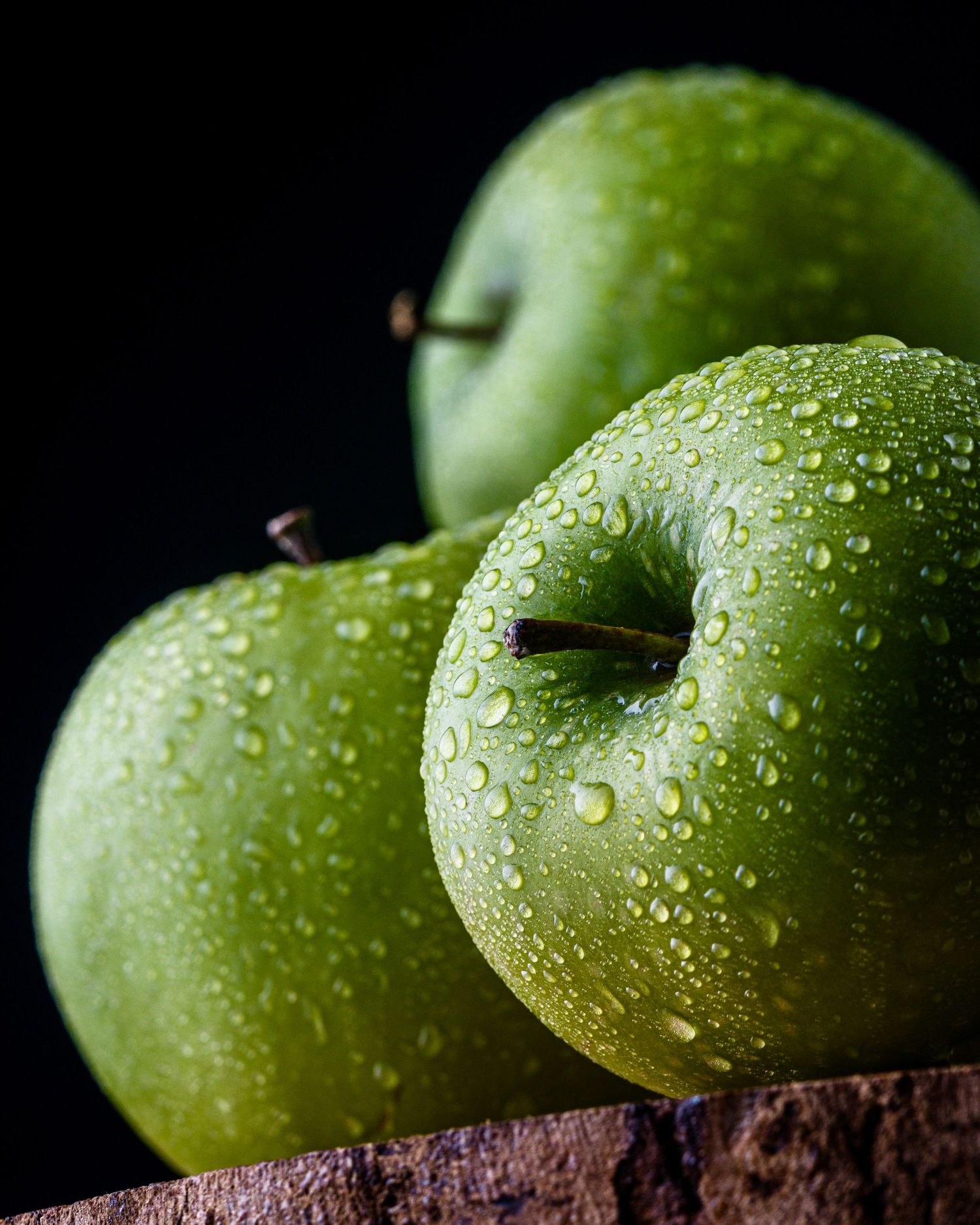 Fresh green Granny Smith apples covered in water droplets on a dark background.