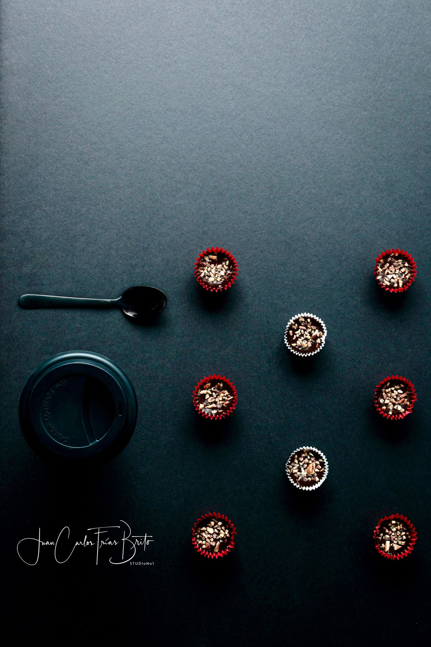 Flat lay of chocolate truffle cups in red liners with a spoon and jar on a dark background.