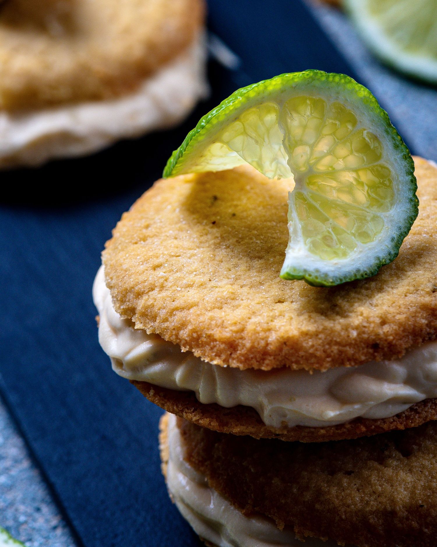 Stacked lime sandwich cookies with cream filling and a lime slice on top.