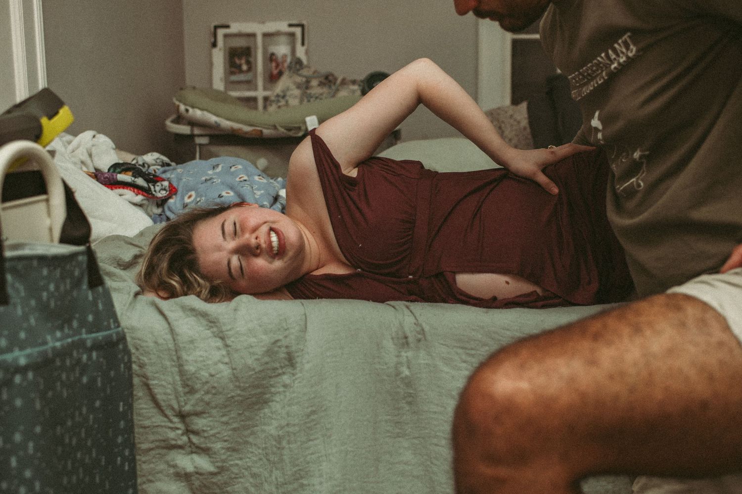 Portsmouth, Virginia mom pushing through a big contraction on a bed in their living room while her husband tries to help.