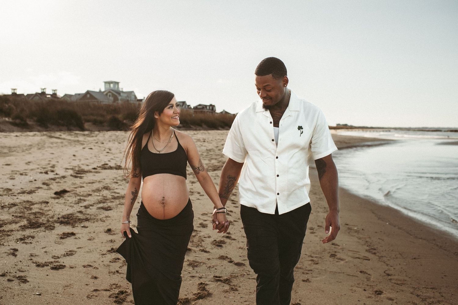 Local expecting couple walk hand in hand on the beach in Virginia Beach during their maternity session.