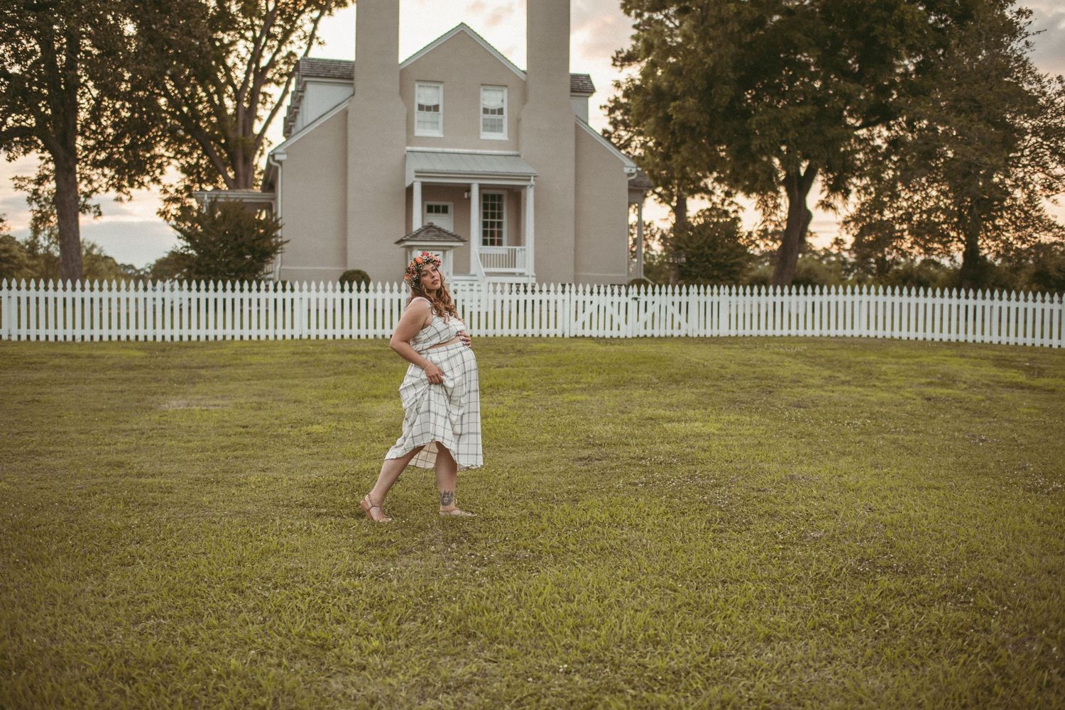 Expecting mother frolicking in a field in front of a beautiful white home at a local Smithfield park.