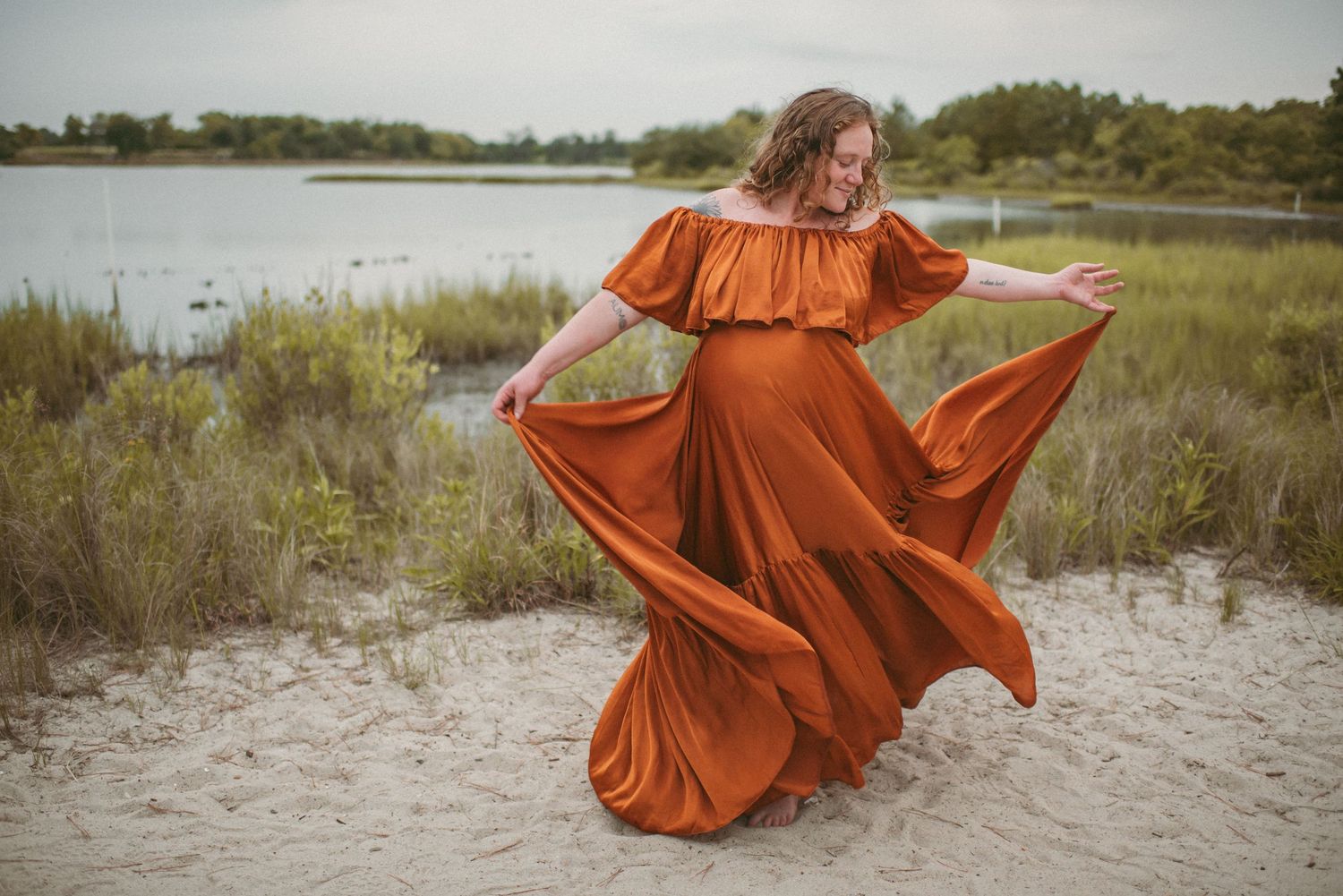 Virginia Beach local mom dances during her maternity session in a bright orange maternity dress.