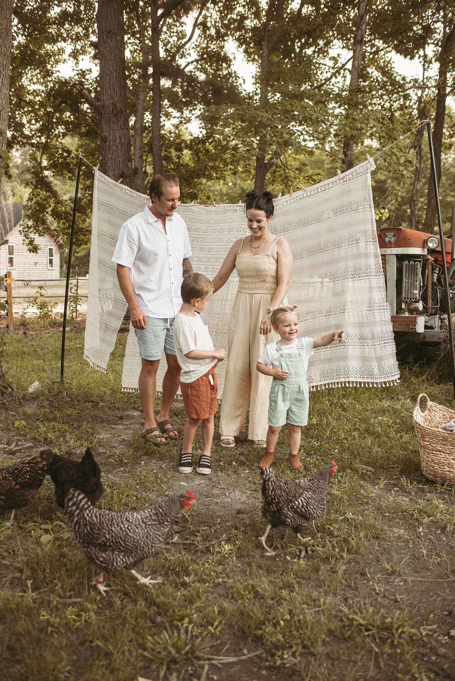 A Virginia family poses together in front of a white tapestry backdrop outdoors with chickens roaming in the foreground.