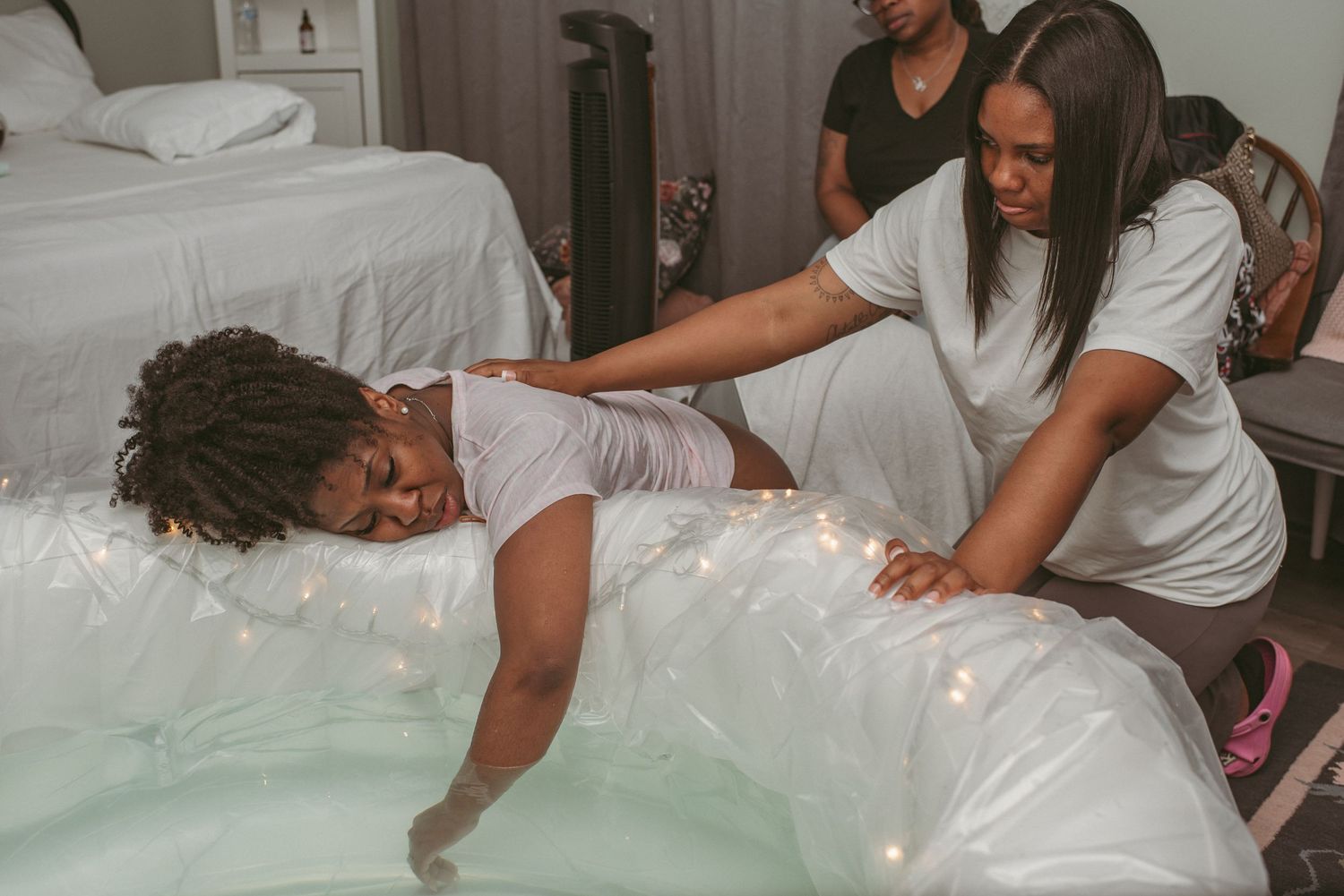 Laboring mother of color leaning on birthing tub while her doula supports her through her contractions at a local birthing center in VA.