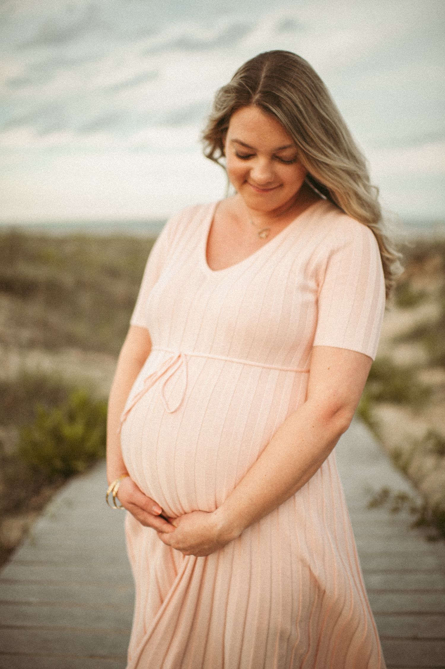 glowing mom to be posing for a maternity photo at the beach in Virginia Beach.