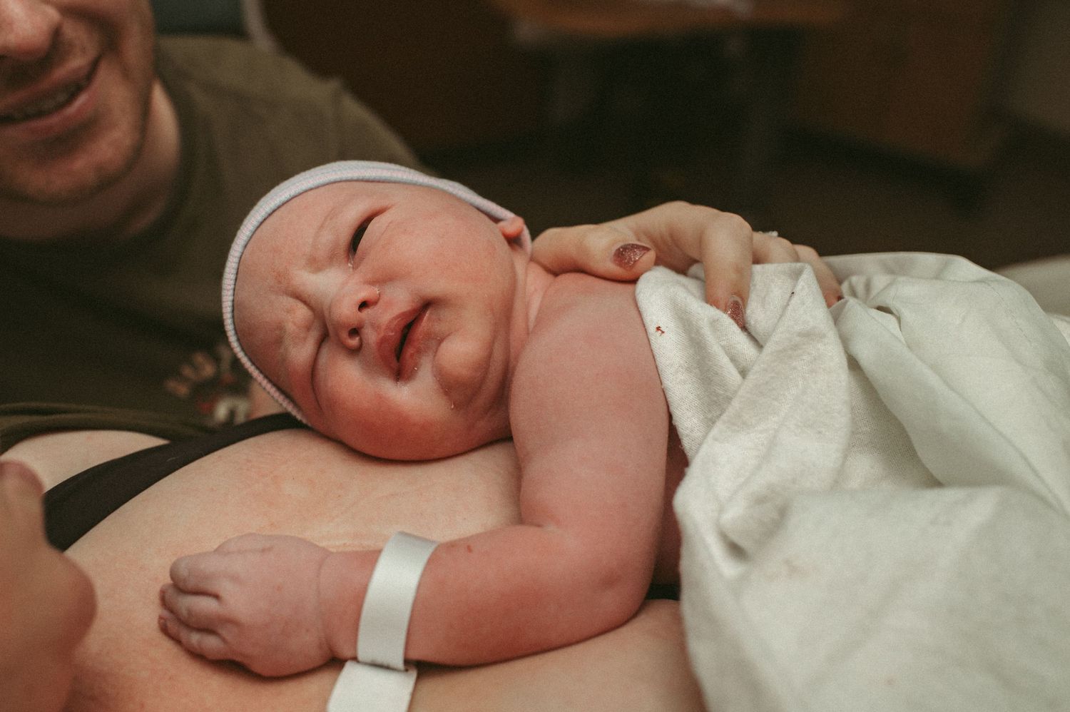 Newborn baby resting on mother's chest after birth, wrapped in white hospital blanket.