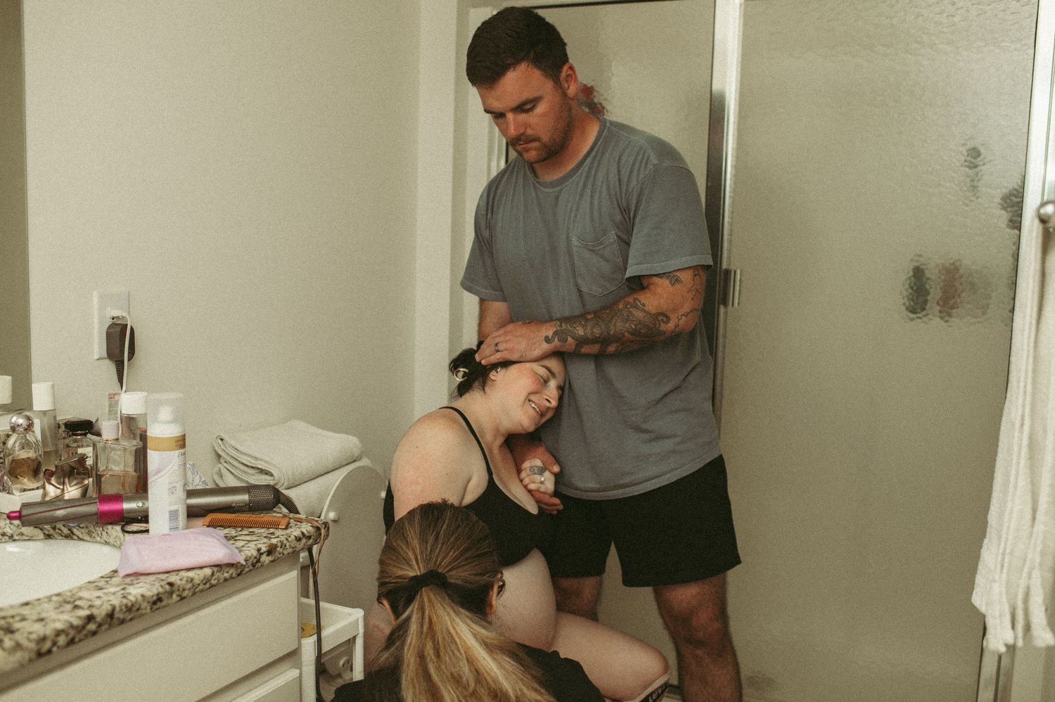 Hampton Roads father rubs his laboring wife's forehead while she sits on their toilet at home.