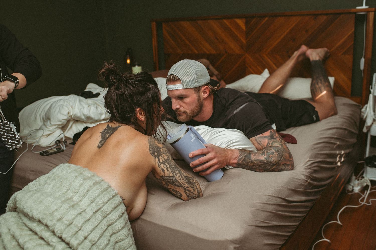 Expecting father gives his laboring wife a sip from her water bottle in between contractions in their bedroom.