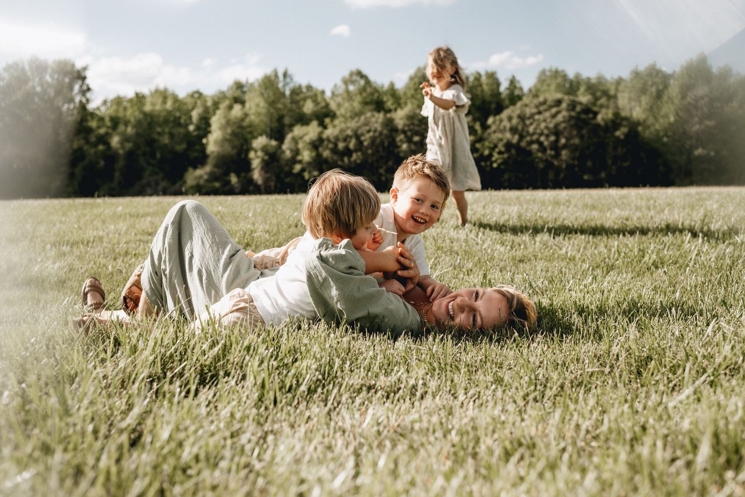 A mother and her boys wrestle on a grassy field while enjoying a beautiful summer day together in Virginia.