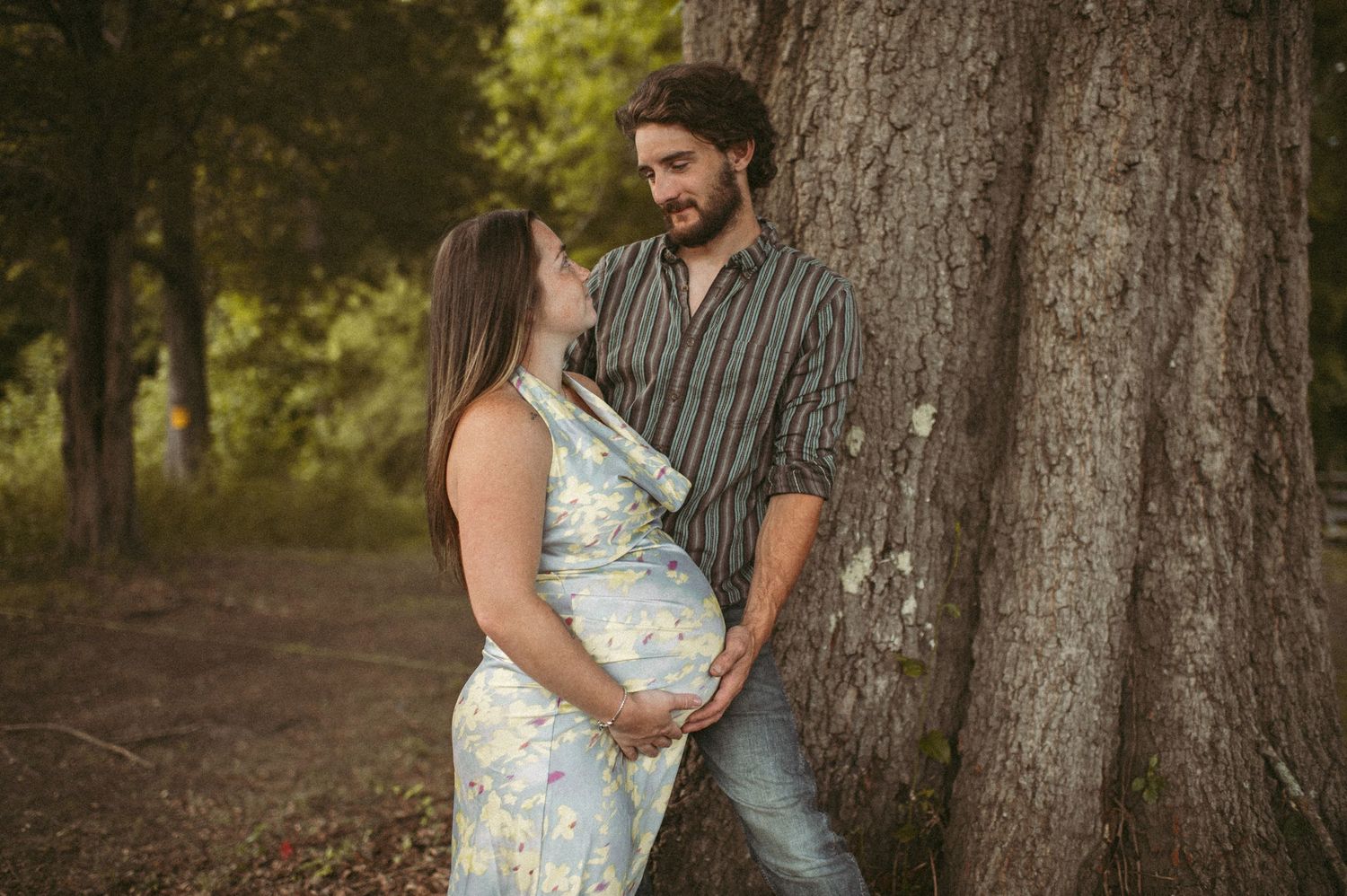 Expecting mother and father staring in each other's eyes in front of their huge tree on their property in Suffolk, Virginia.
