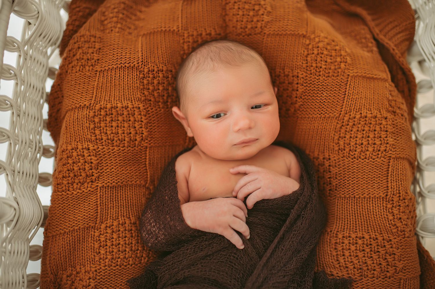 Baby boy laying in a white basket and on top of an rusty orange blanket at a Chesapeake, Virginia studio.