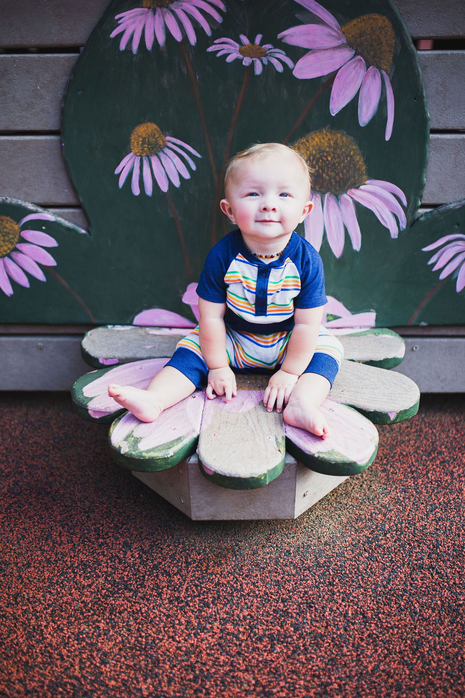 Baby boy sitting on a playground wooden flower at a local playground.