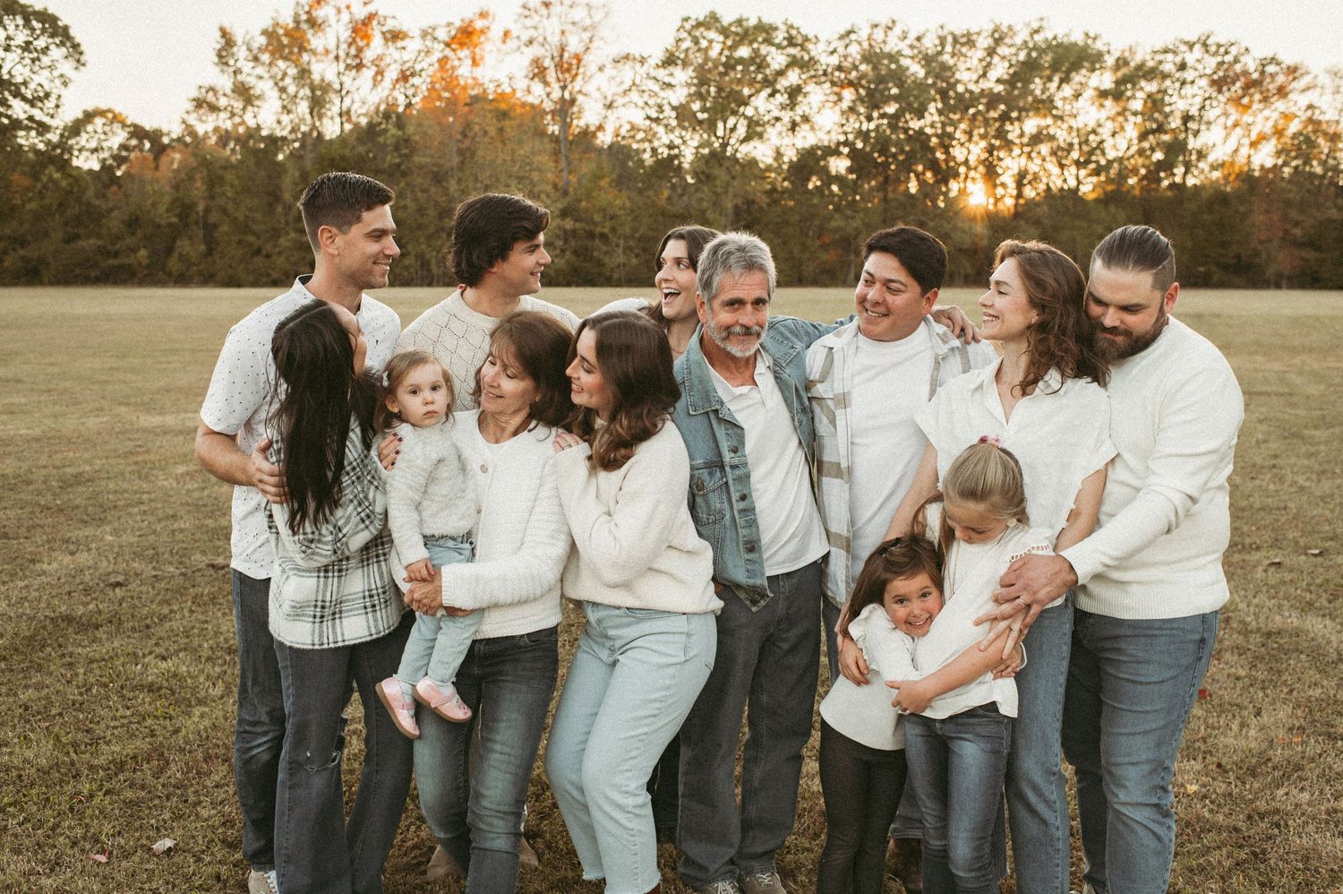 extended family session wearing coordinating white and denim outfits laughing together in a grassy field at sunset in a Suffolk, VA park.