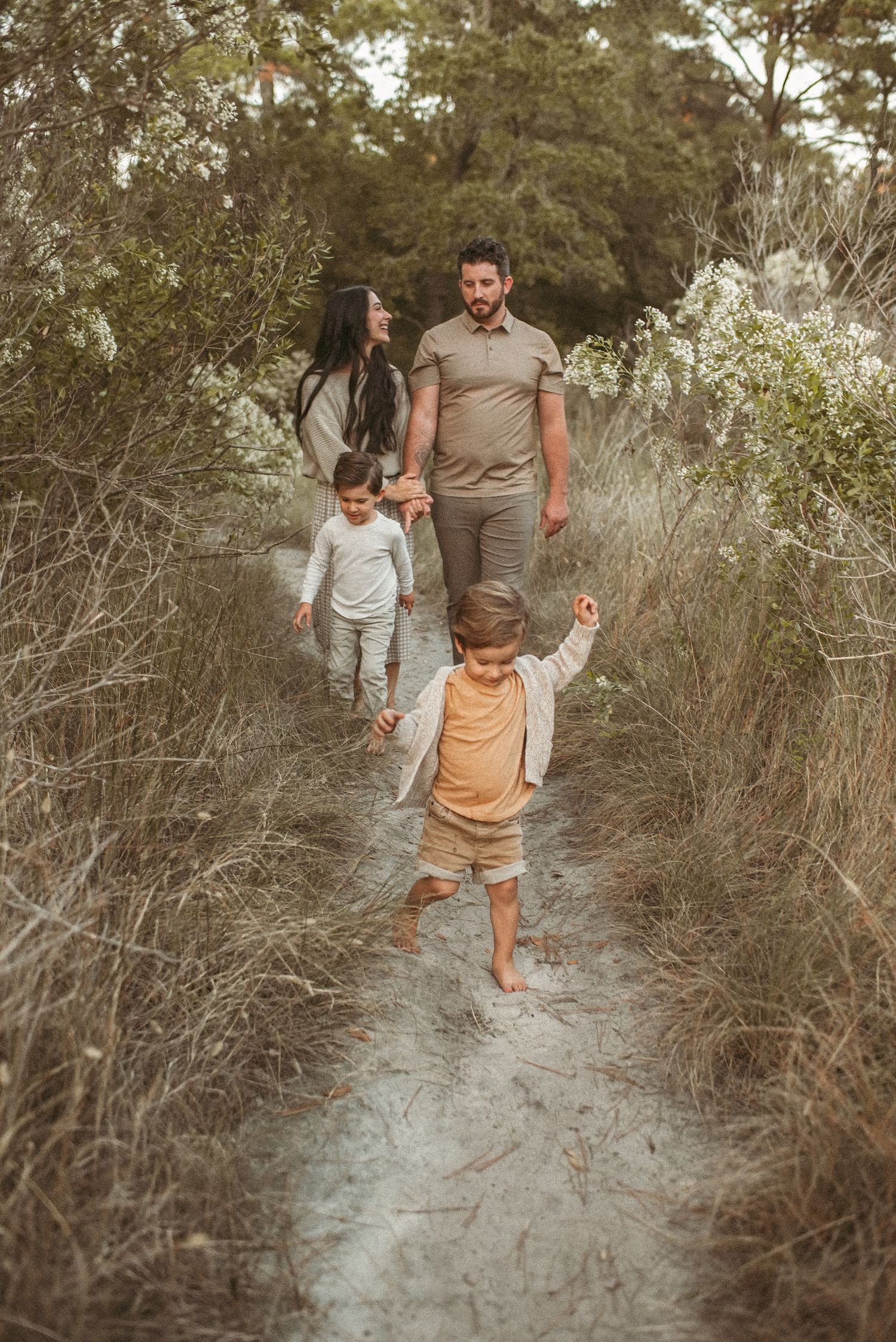 Parent and child walk together holding hands along a sandy nature trail in Virginia Beach.