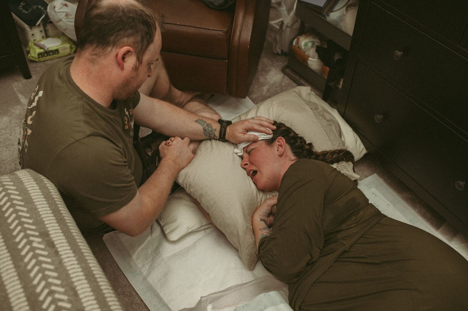 Husband places cold wash cloth on his wife while she labors on the floor in their home in Virginia.