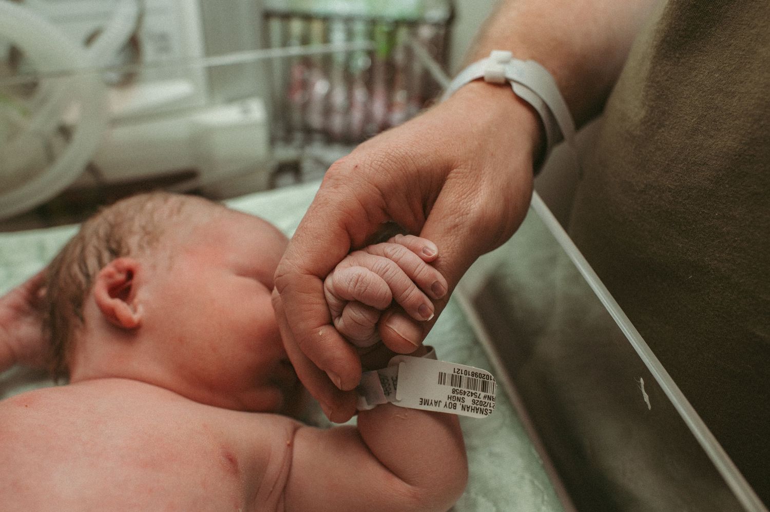 New Father tenderly holds baby boys hand while he is being examined by the hospital pediatrician in Norfolk.