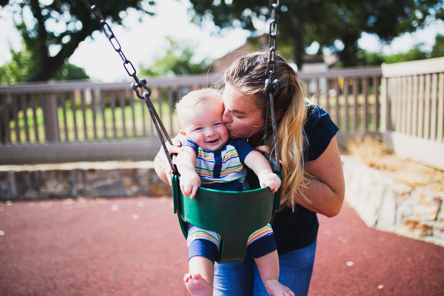 mom kisses son while swinging in a baby swing at a local playground.