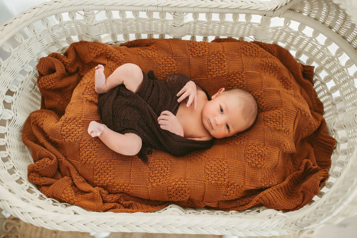 Newborn boy being posed in a white basket at a Chesapeake studio.
