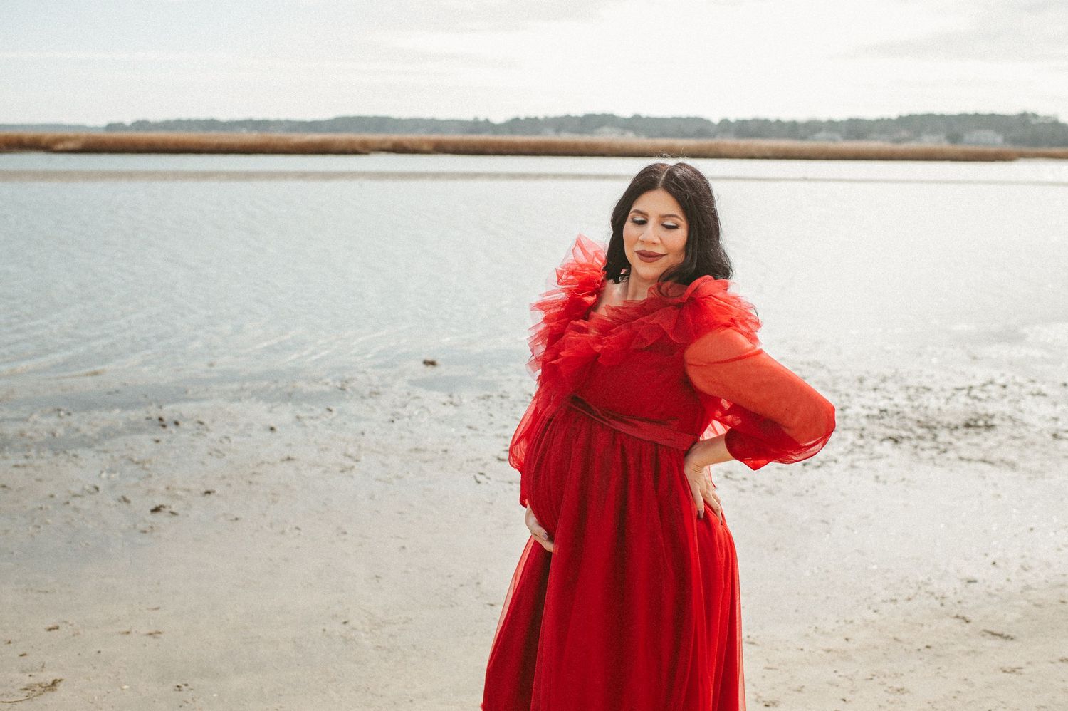 Expecting mother in a red dress posing on a beach in Virginia Beach, Virginia.