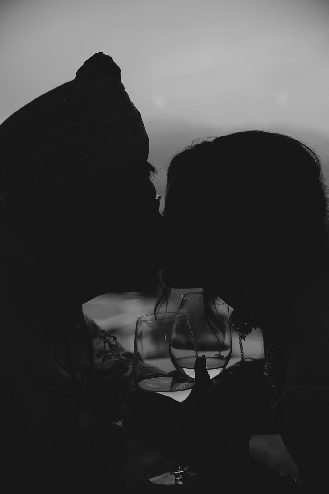 Romantic black and white silhouette of couple about to kiss at dusk holding wine glasses.