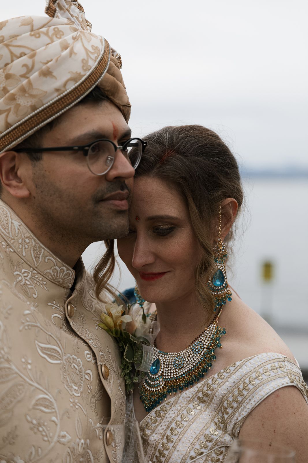 Couple in traditional Indian wedding attire, groom in cream sherwani with turban and bride in embroidered lehenga.