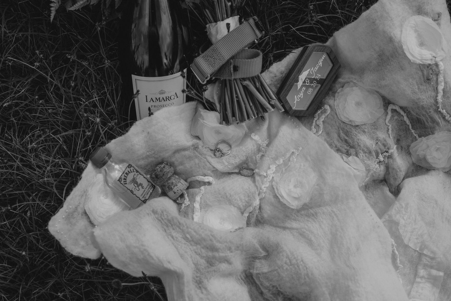 A black and white flatlay of a soft blanket, a bottle of Lamarca, bouquet of wildflowers wrapped with a memorable dog collar.