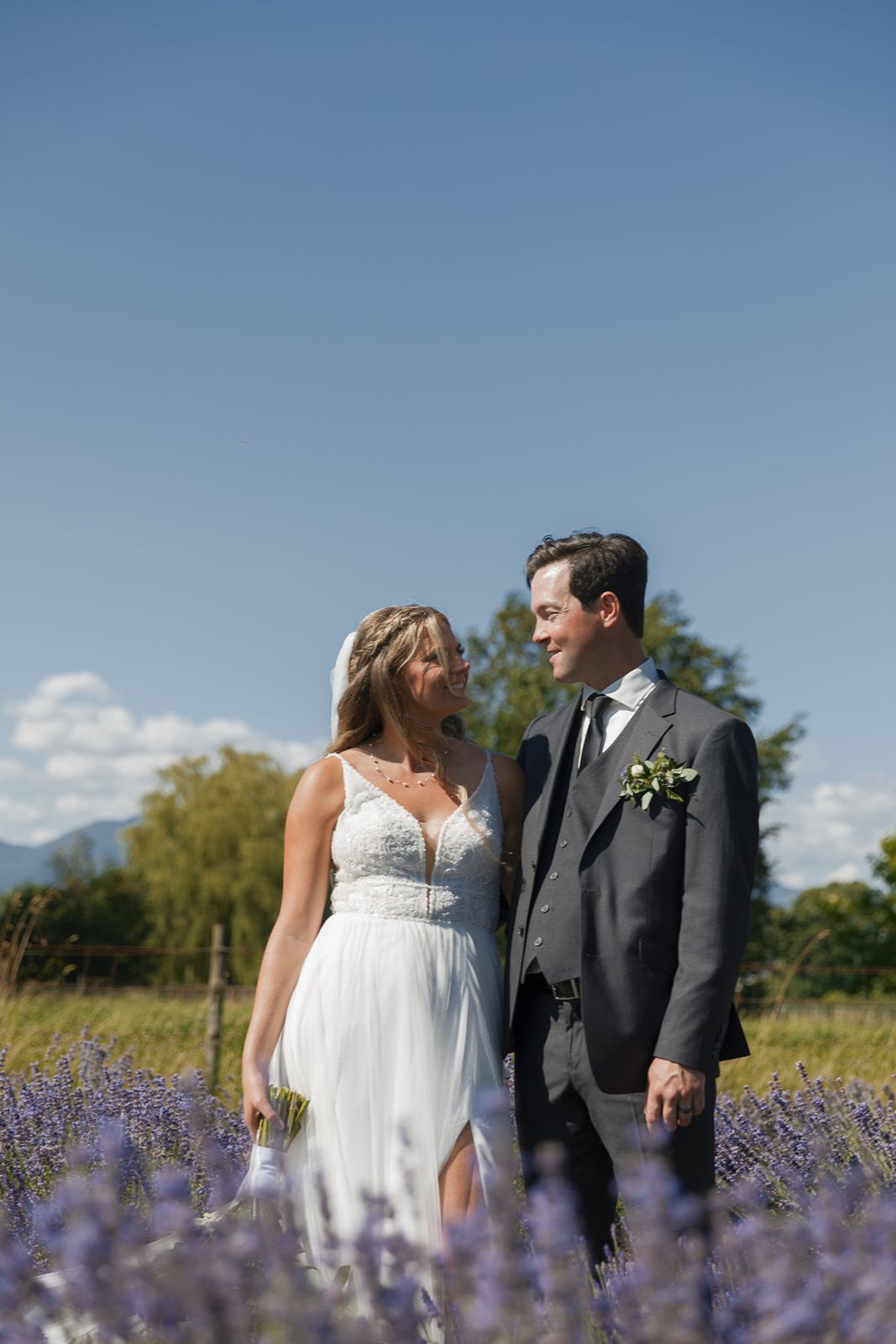Bride and groom share a romantic moment in a blooming lavender field under a bright blue sky.