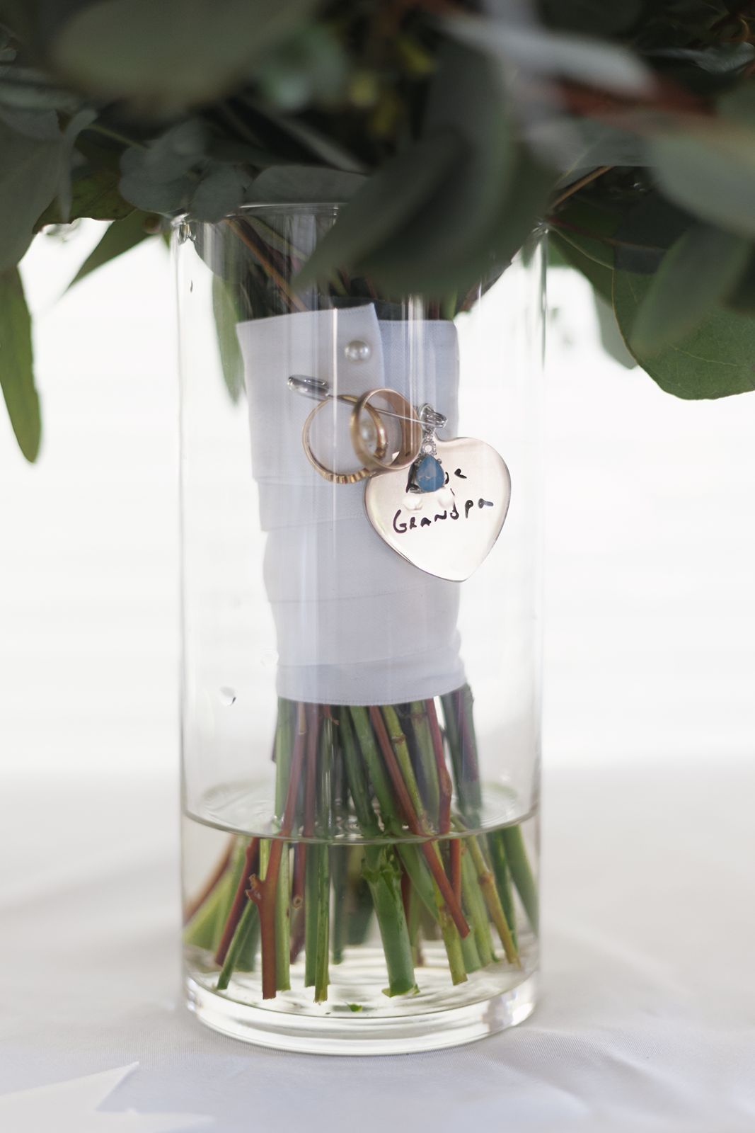 Bridal bouquet displayed in glass vase with wedding rings and Grandpa memorial heart charm keepsake.