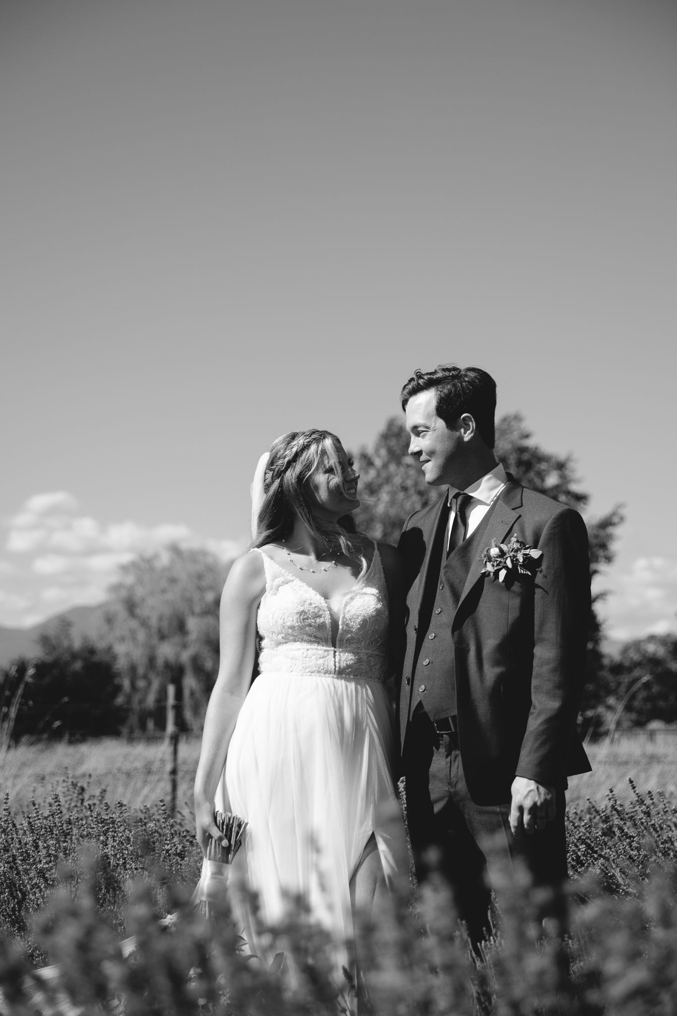 Elegant black and white portrait of bride and groom smiling at each other in a sunlit field.