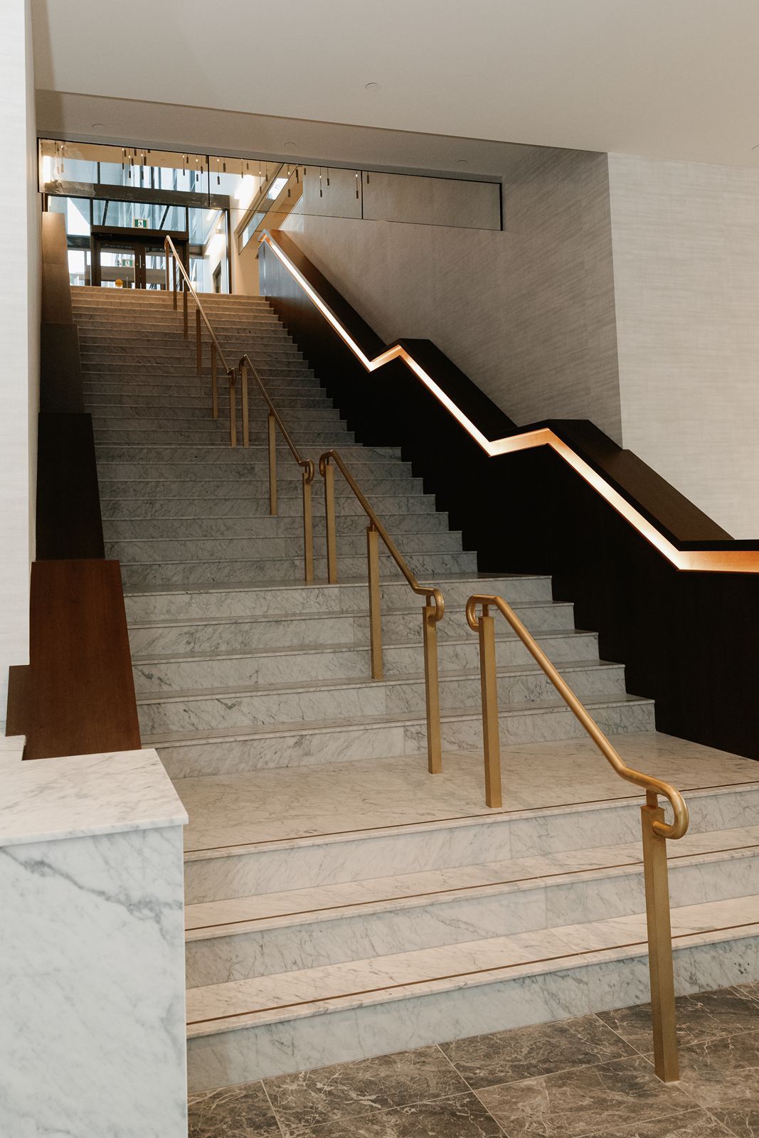 Grand marble staircase with gold handrails and illuminated steps in an elegant building interior.