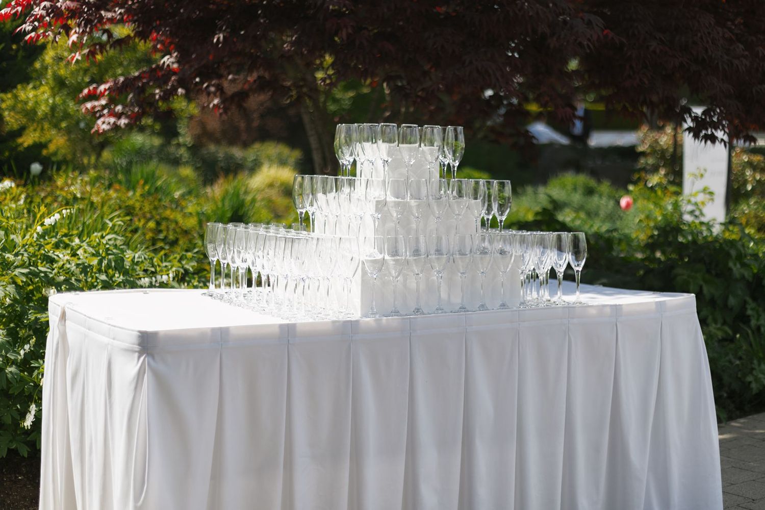 Elegant pyramid tower of champagne and wine glasses stacked on a white skirted table in a garden wedding setting.