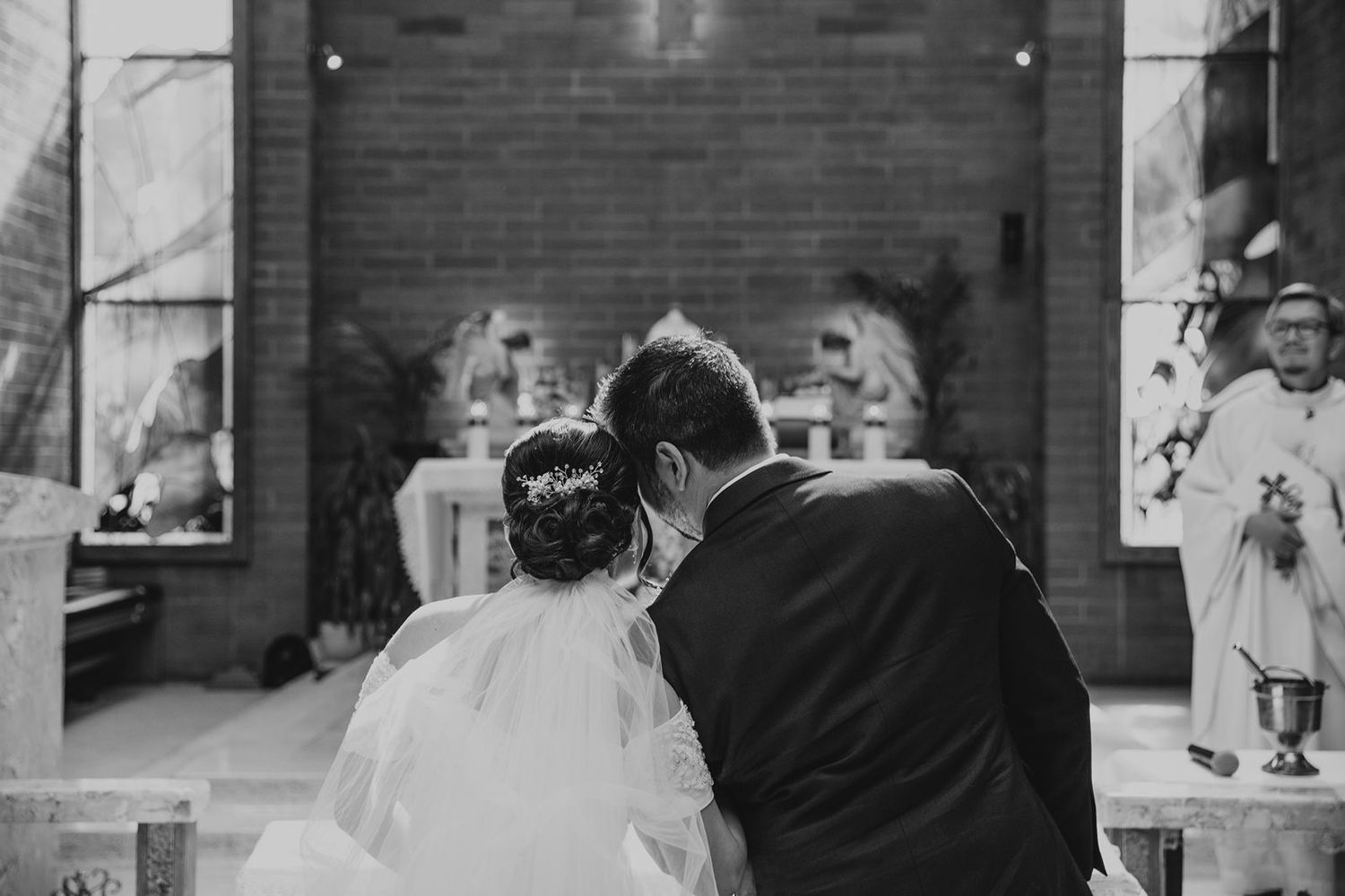 Black and white photo of bride and groom kneeling together at a church wedding altar.