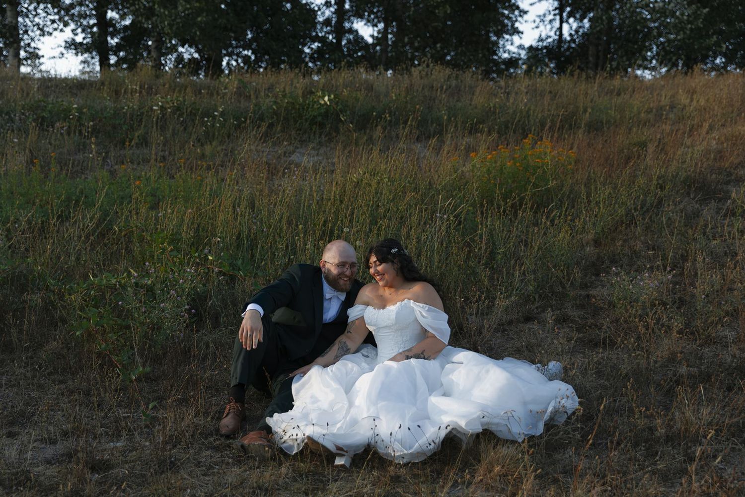 Bride and groom sitting together in a golden field, sharing an intimate moment in wedding attire.