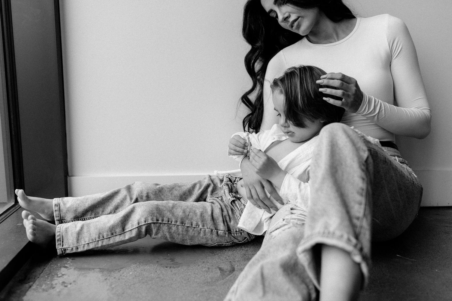 Candid moment of Kristina and her young son cuddled on a sunlit floor beside a window, authentic and warm connection.