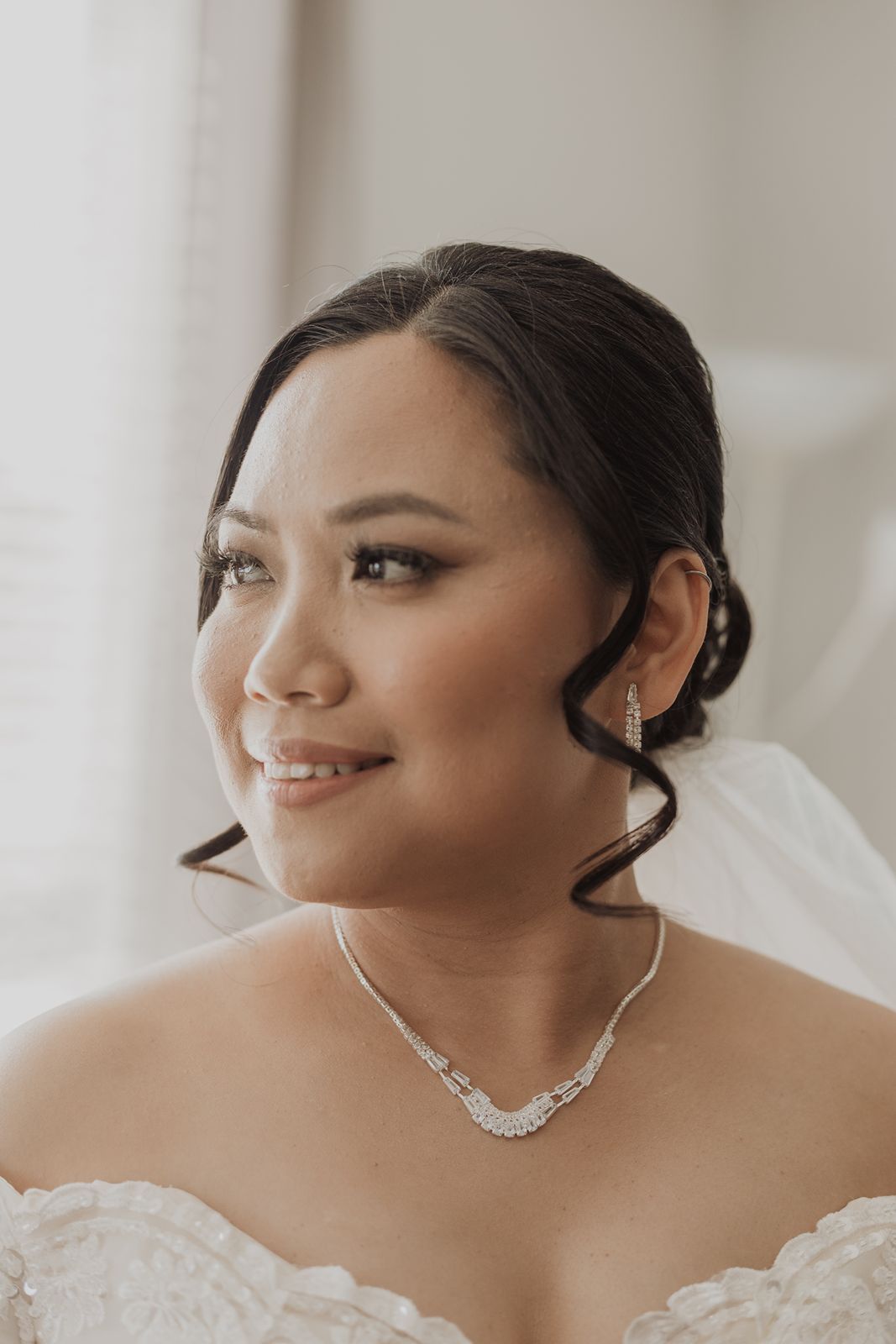 Beautiful bride in white gown wearing diamond necklace and earrings on her wedding day.